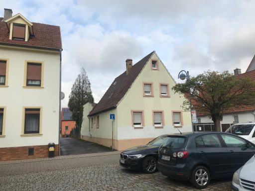 Zwei Wohnhäuser an einer ruhigen Straße, grauer Himmel, parkende Autos.