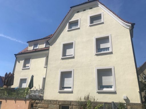 Helles mehrstöckiges Gebäude mit Giebeldach und weißen Fensterläden.