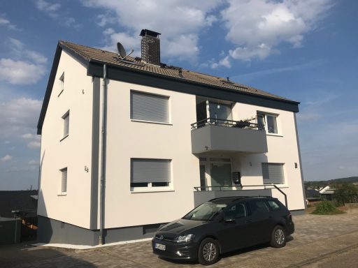 Helles, dreigeschossiges Wohnhaus mit Balkon und Parkplatz für ein Auto.